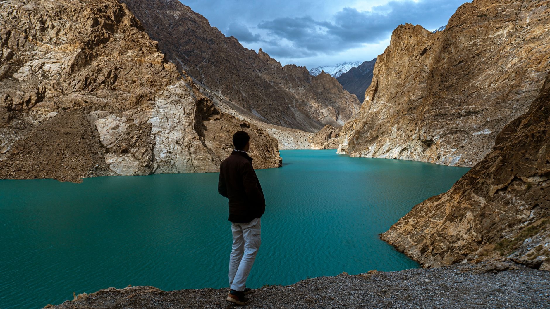 A man gazes at the stunning turquoise waters of Attabad Lake surrounded by majestic mountains in Hunza, Pakistan.
